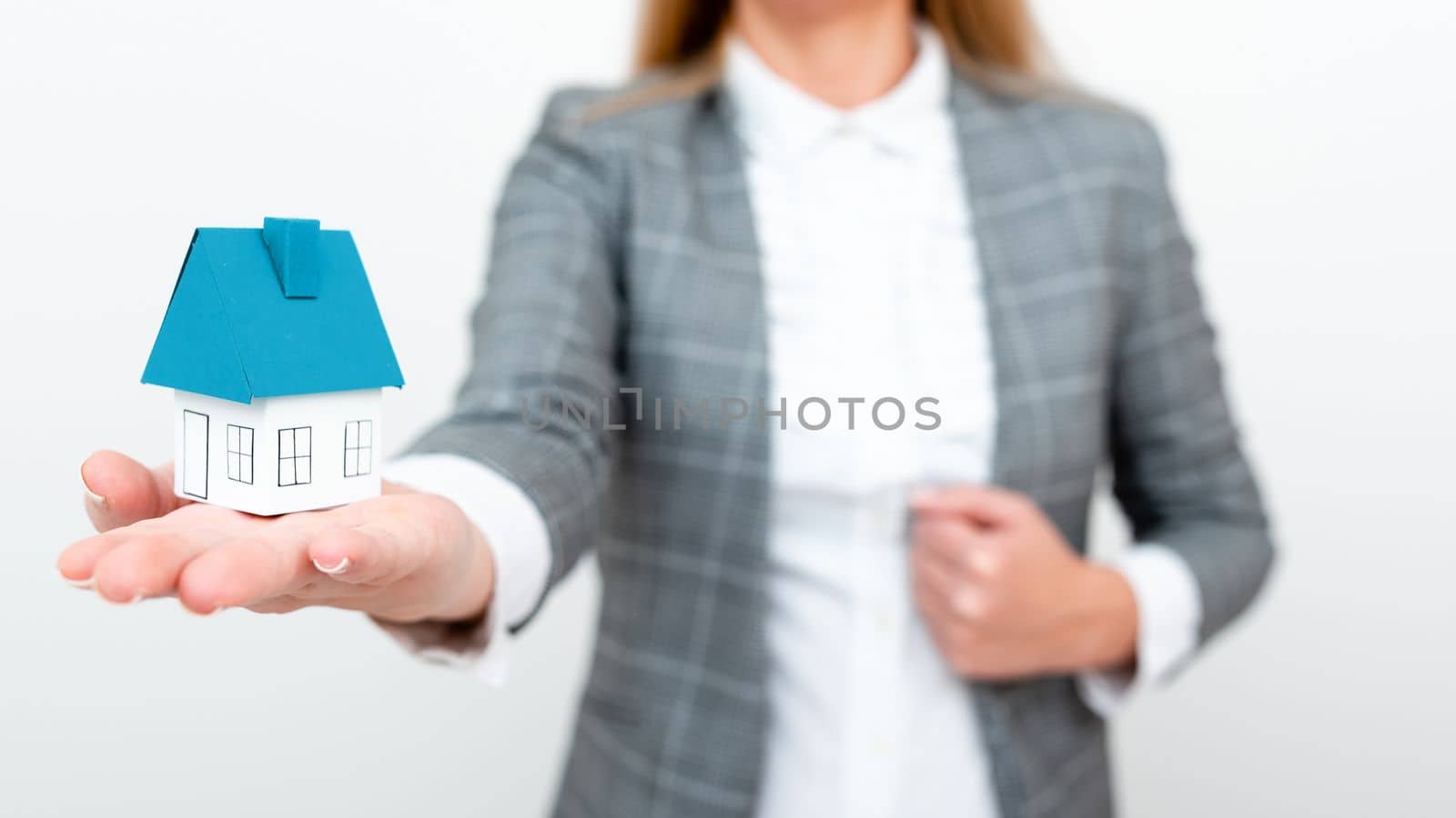 Businesswoman in gray suit holding colored paper house in one hand. Showing Important Informations. Executive Displaying Late News. Woman Showing Recent Updates. by nialowwa