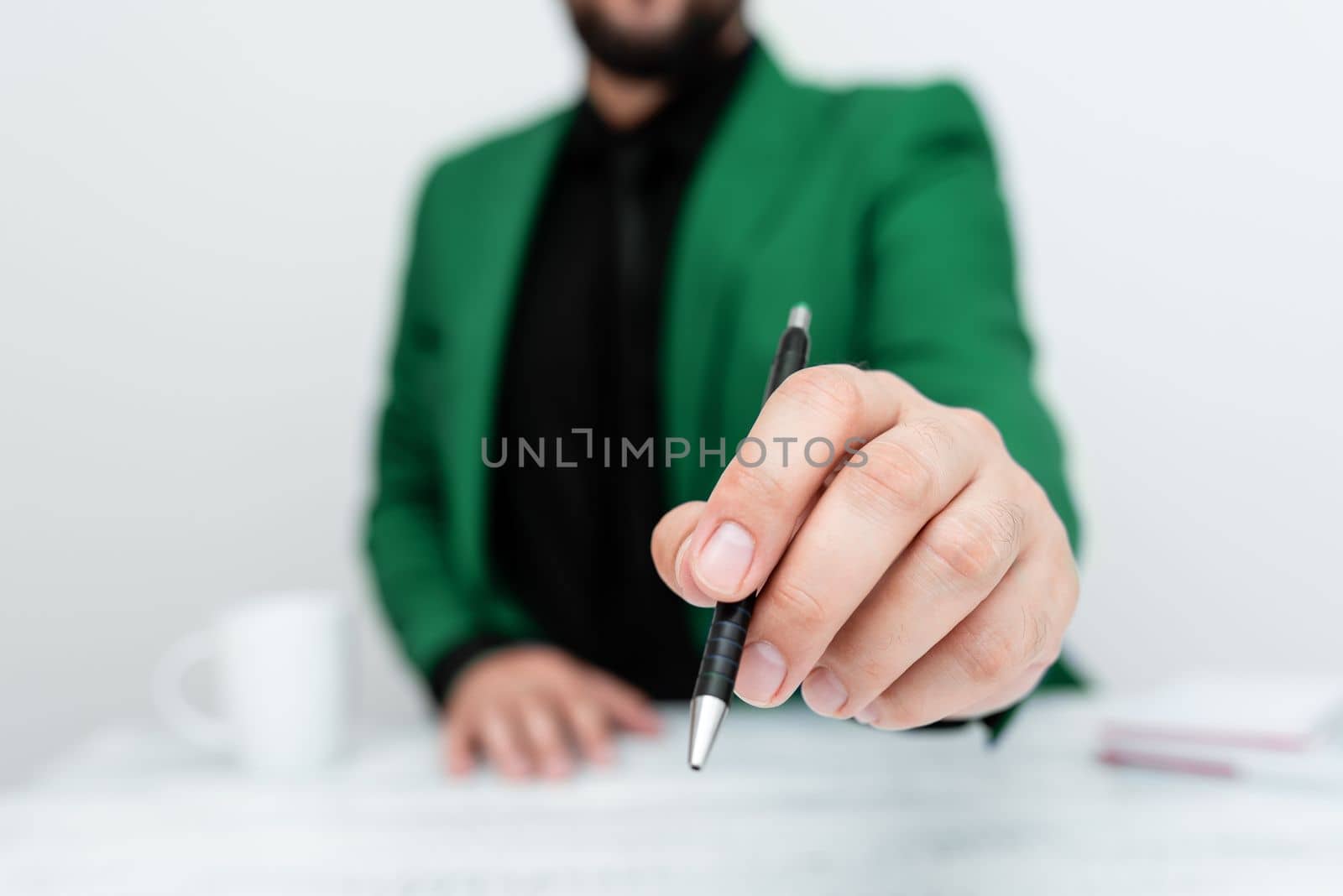 Male model in Green suit sitting at white table And Pointing With Pen On Important Message. Gentleman Showing Critical Announcement. Coffee cup on deck. by nialowwa