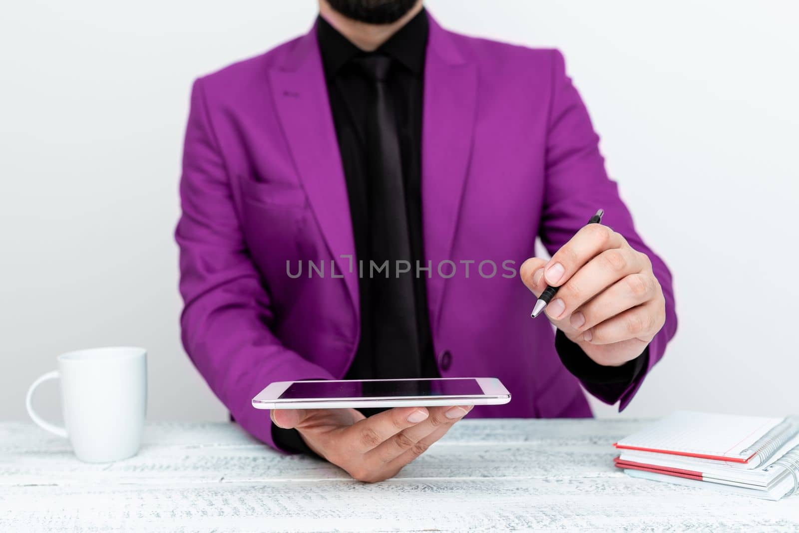 Man in Pink jacket sitting at white table And Pointing With Pen On Important Message. Holding mobile phone. Gentleman Showing Critical Announcement. by nialowwa