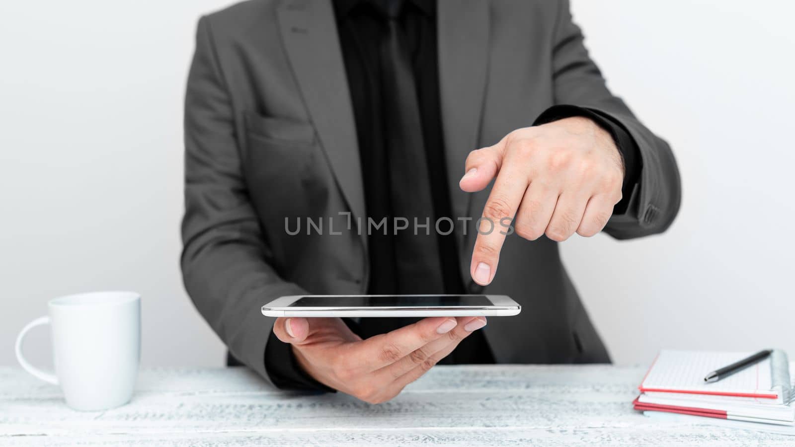 Businessman in gray jacket sitting at table holding mobile phone And Pointing With One Finger On Important Message. Gentleman Showing Critical Announcement. by nialowwa