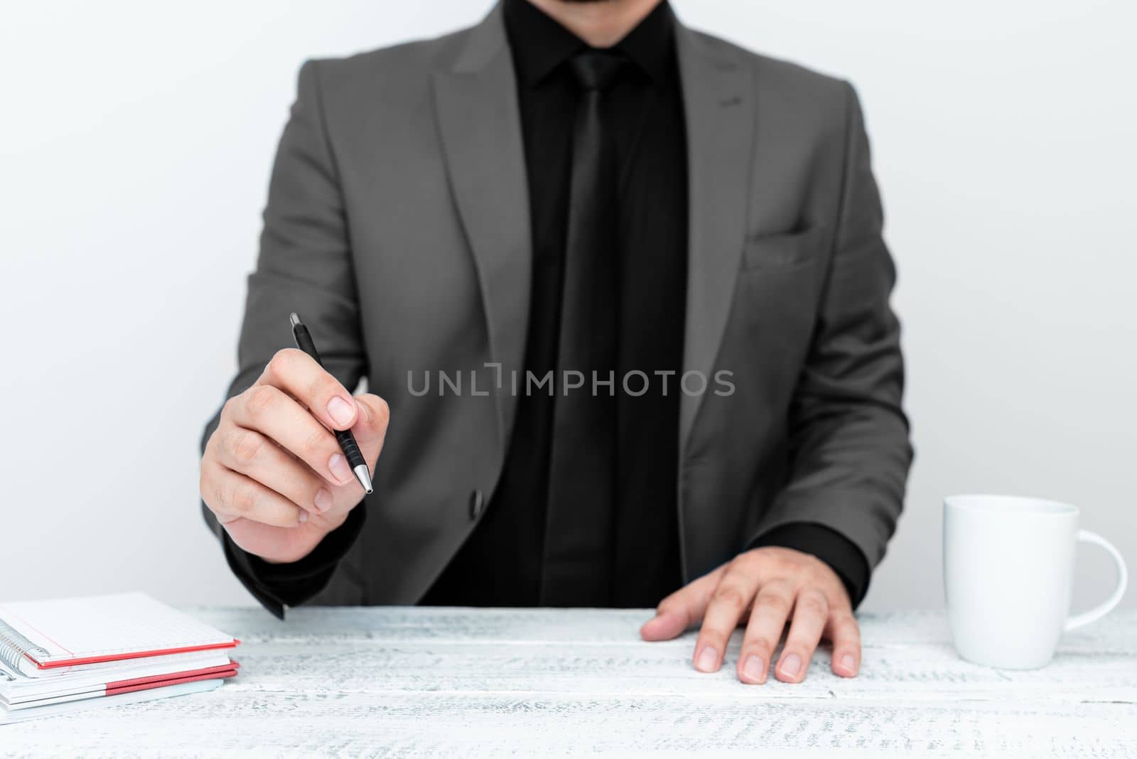 Male model in Gray suit sitting at white table And Pointing With Pen On Important Message. Gentleman Showing Critical Announcement. Coffee cup on deck. by nialowwa