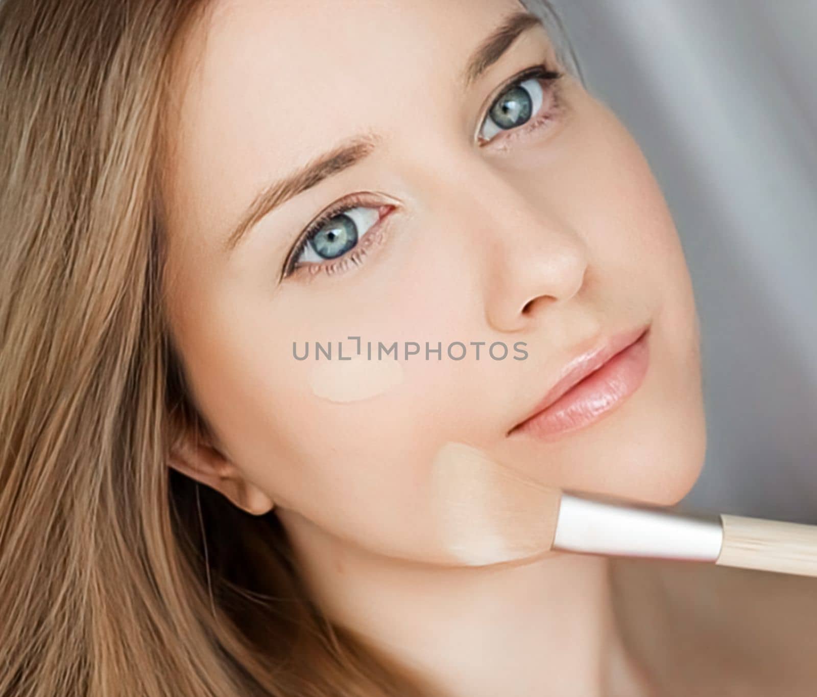 Beautiful woman applying liquid make-up foundation on her skin with make-up brush.