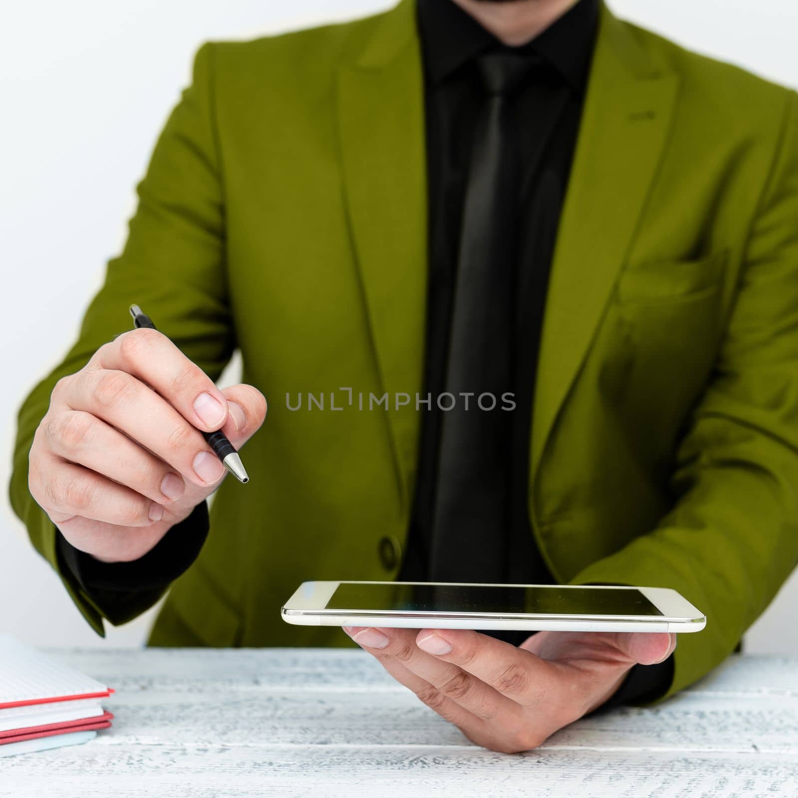 Man in Green jacket sitting at white table And Pointing With Pen On Important Message. Holding mobile phone. Gentleman Showing Critical Announcement. by nialowwa