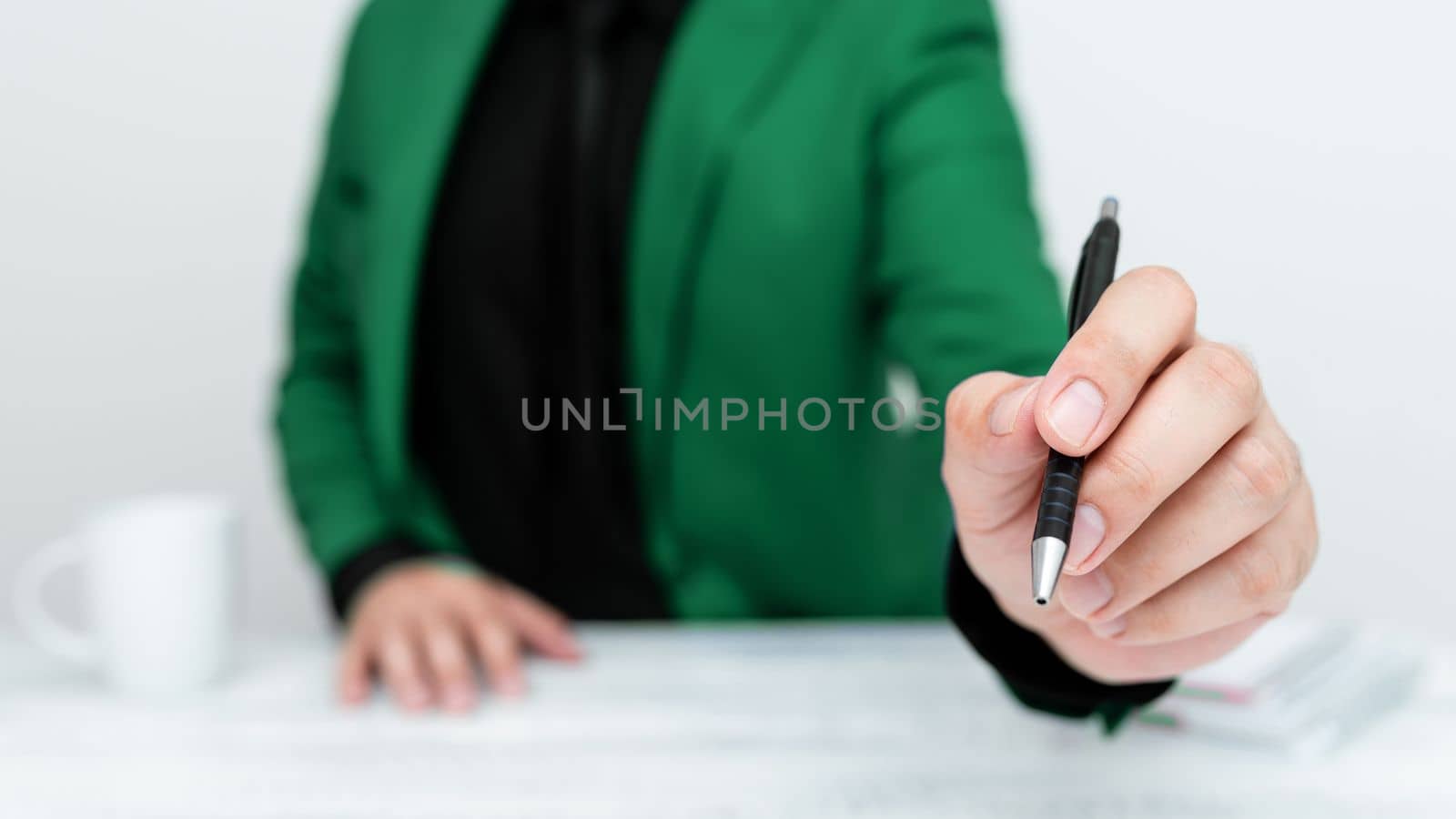 Male model in Green suit sitting at white table And Pointing With Pen On Important Message. Gentleman Showing Critical Announcement. Coffee cup on deck. by nialowwa