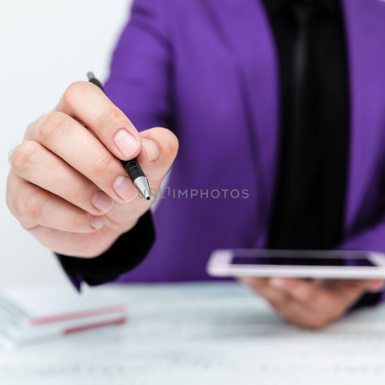 Man in Purple jacket sitting at white table And Pointing With Pen On Important Message. Holding mobile phone. Gentleman Showing Critical Announcement. by nialowwa