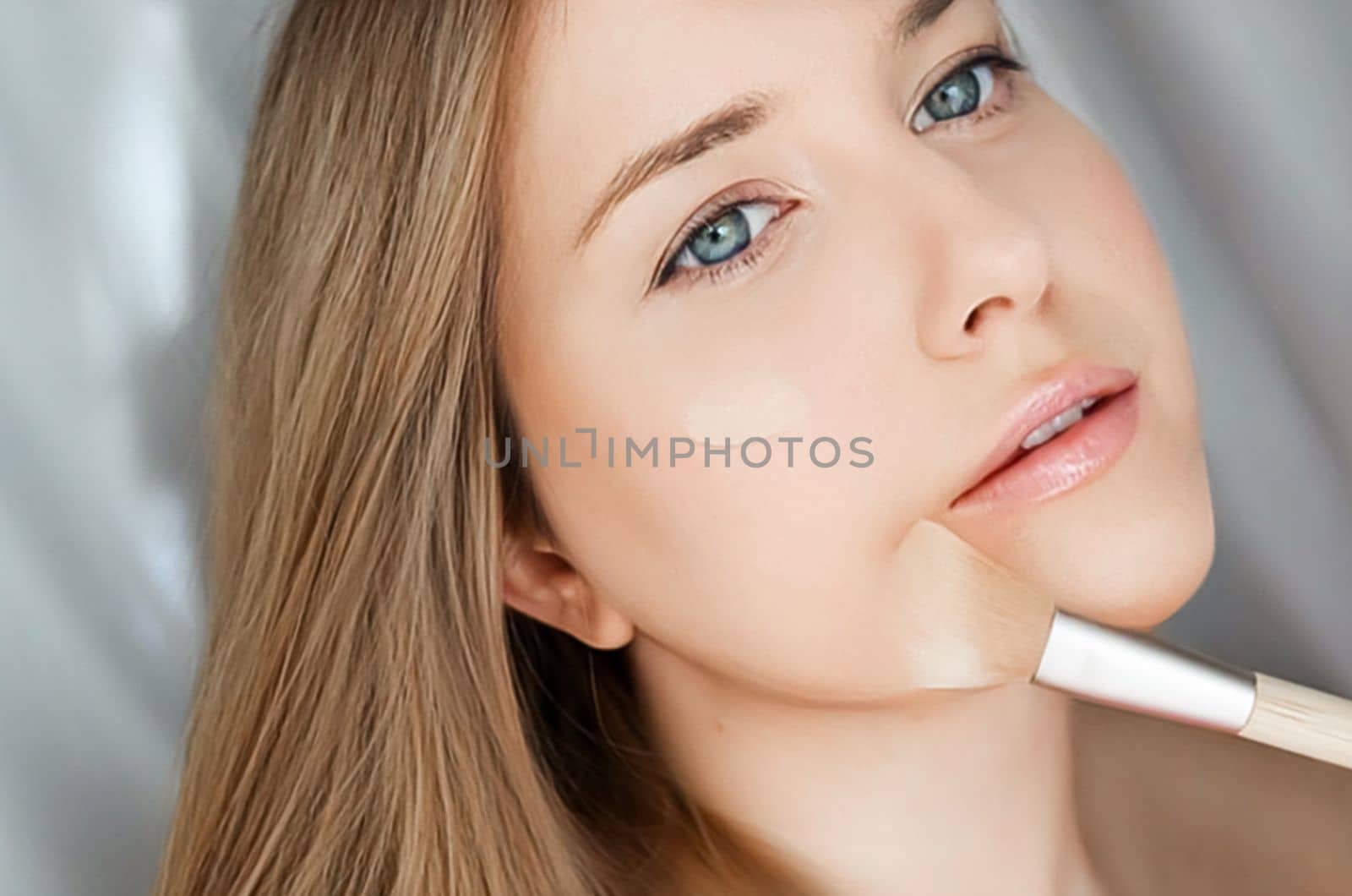 Beautiful woman applying liquid make-up foundation on her skin with make-up brush.