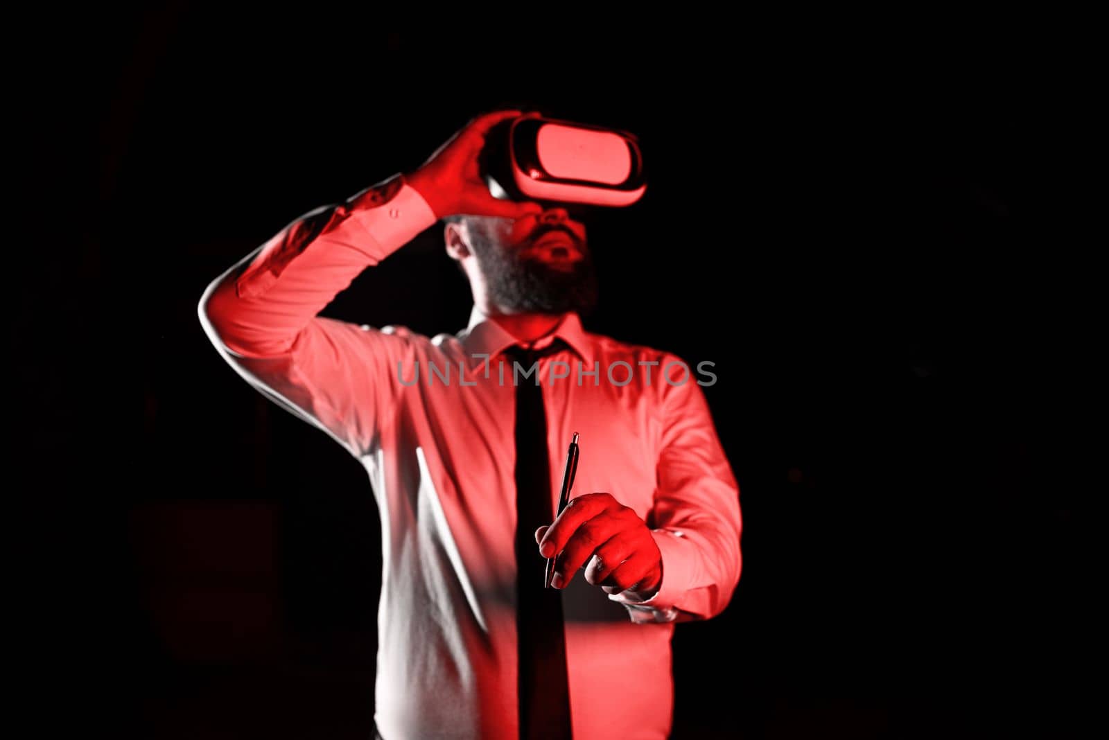 Standig Man Holding Pen To Point Important Messages And Wearing Vr Glasses. Businessman Having Virtual Reality Eyeglasses And Pointing On Crutial Informations. by nialowwa