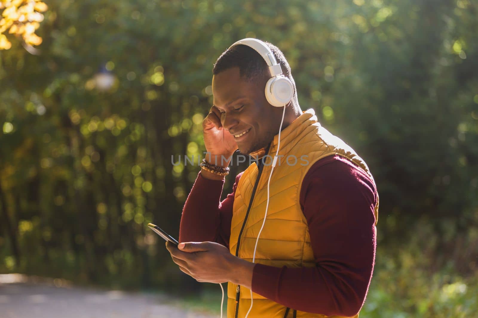 Portrait African american man listens music in autumn park background copy space. Gadget, app and streaming service concept by Satura86