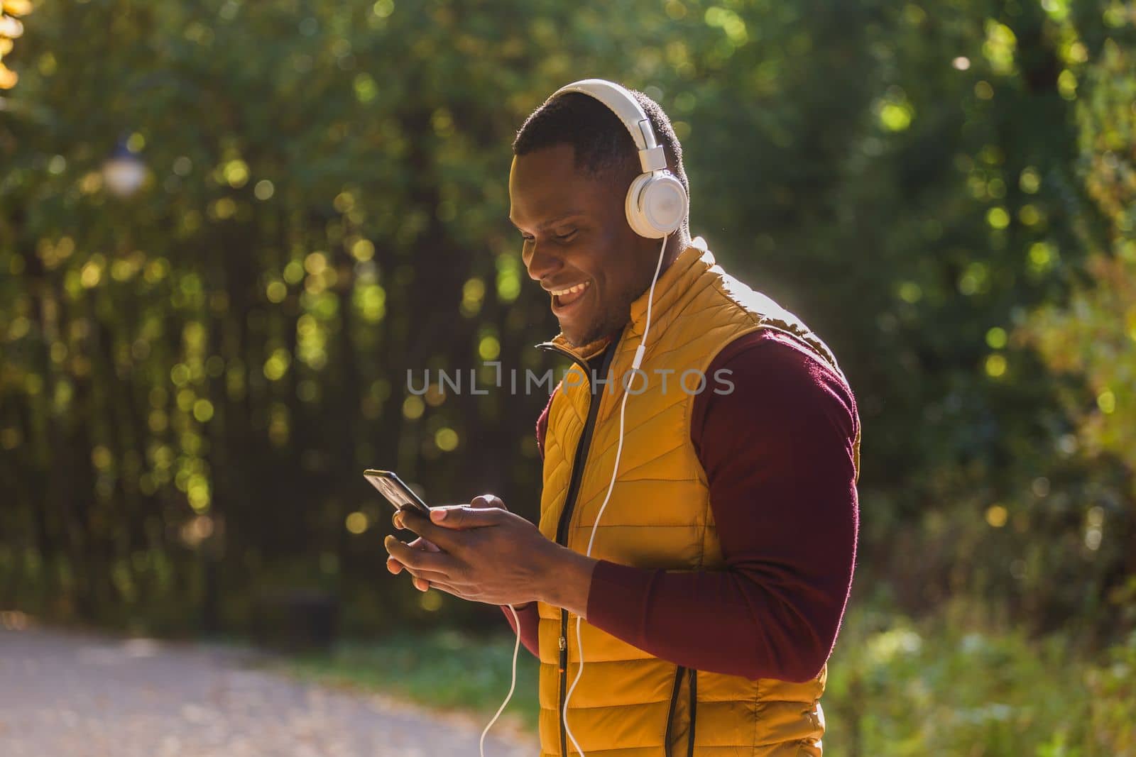 Portrait African american man listens music in autumn park copy space and place for text. Gadget, app and streaming service concept by Satura86