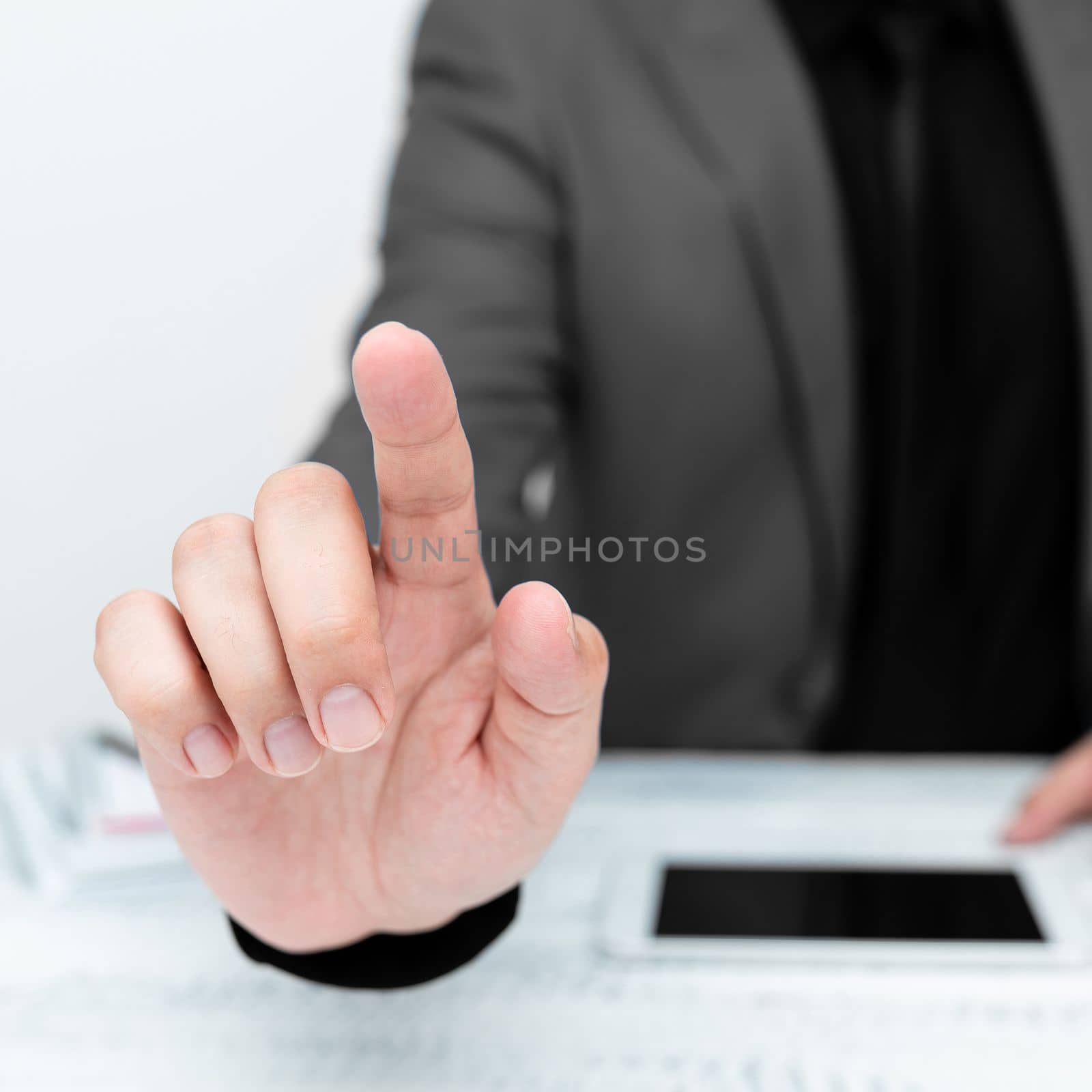 Businessman in Gray jacket sitting at table And Pointing With One Finger On Important Message. Gentleman Showing Critical Announcement. Phone on table. by nialowwa