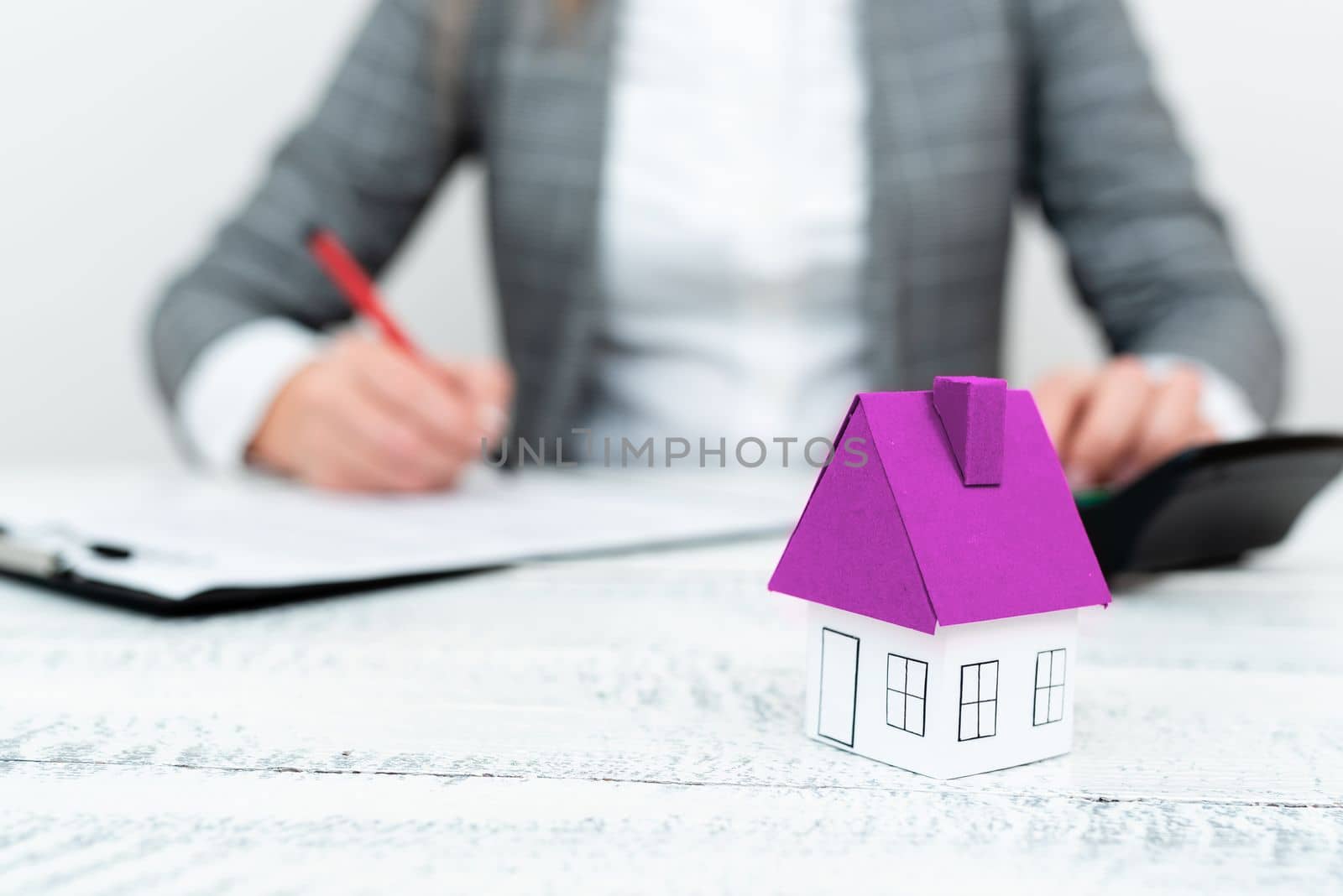 Businesswoman sitting at table and writing in notebook. olored paper house standing on desk. Display important information. Executive Display the latest news. by nialowwa