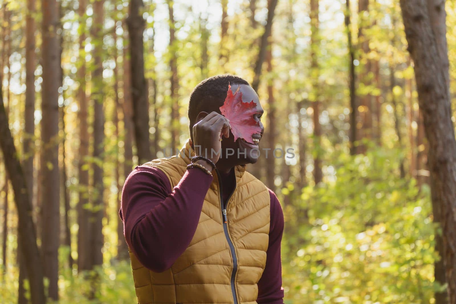Portrait of african american man covering his face with autumn maple leaf. Autumn nature. Seasonal fall fashion. by Satura86