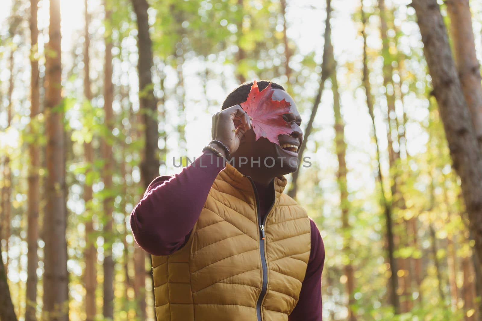 Portrait of african american man covering his face with autumn maple leaf. Autumn nature. Seasonal fall fashion. by Satura86