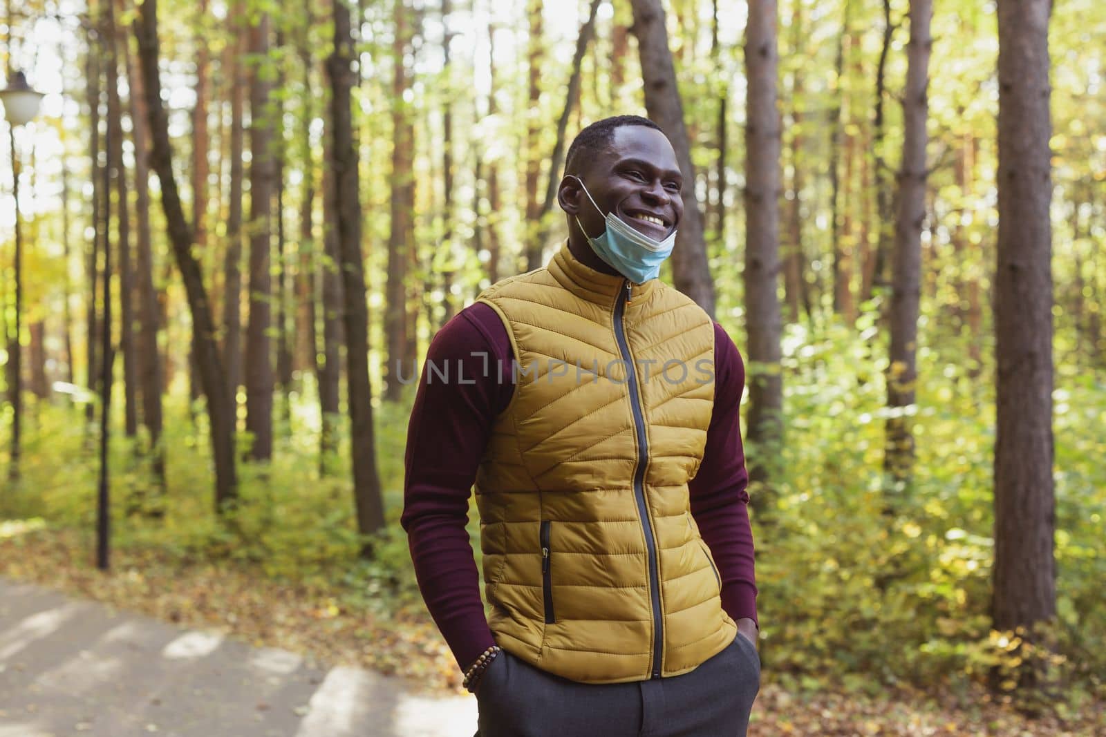 Handsome african american man wearing casual clothes and medical mask smiling happy walking in city park - end pandemic