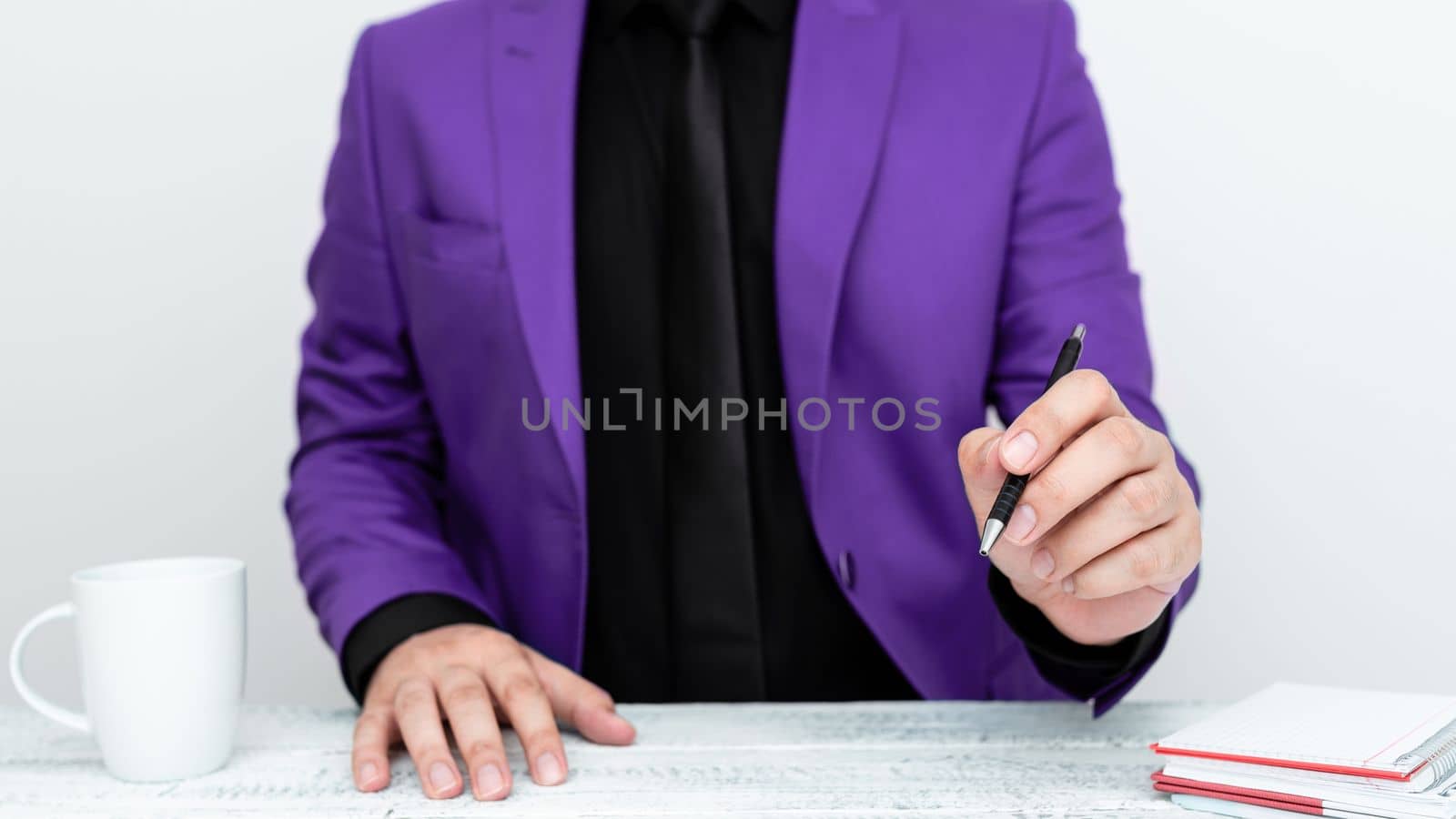 Male model in Purple suit sitting at white table And Pointing With Pen On Important Message. Gentleman Showing Critical Announcement. Coffee cup on deck. by nialowwa