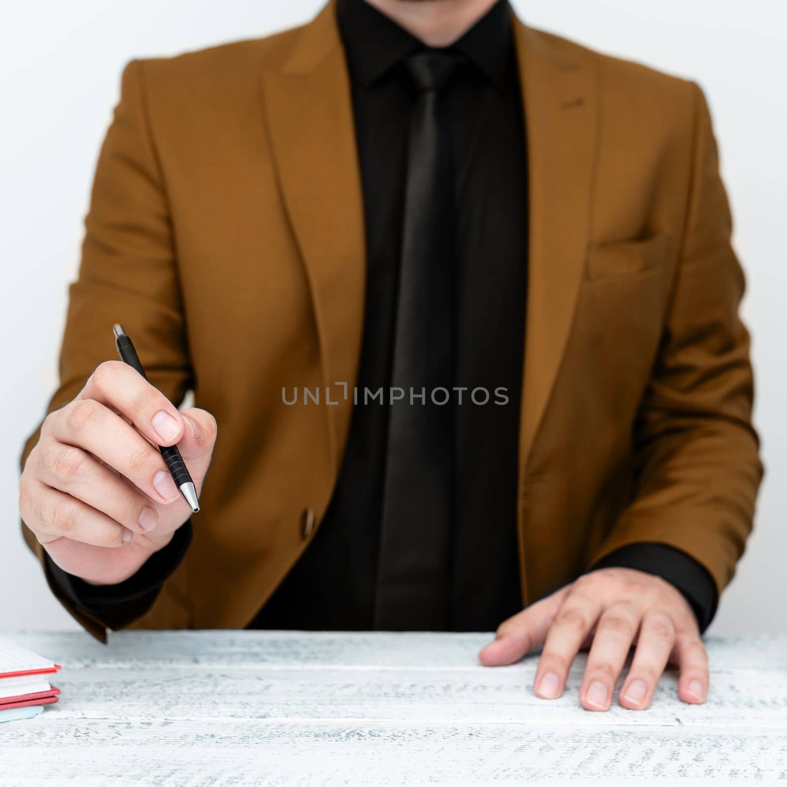 Male model in Brown suit sitting at white table And Pointing With Pen On Important Message. Gentleman Showing Critical Announcement. Coffee cup on deck. by nialowwa