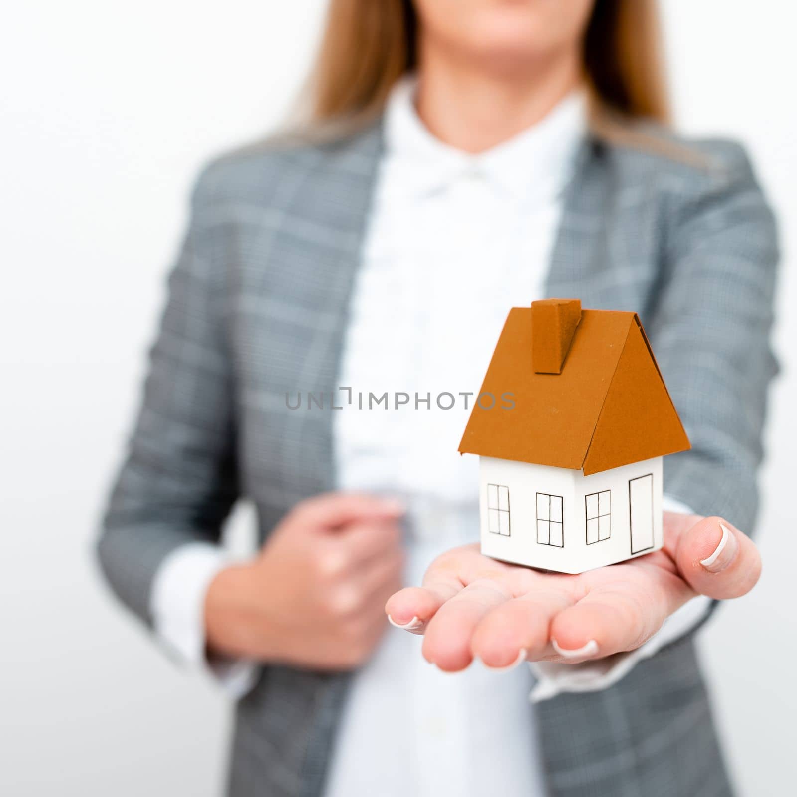 Businesswoman in a gray suit holding a colored paper house in one hand.