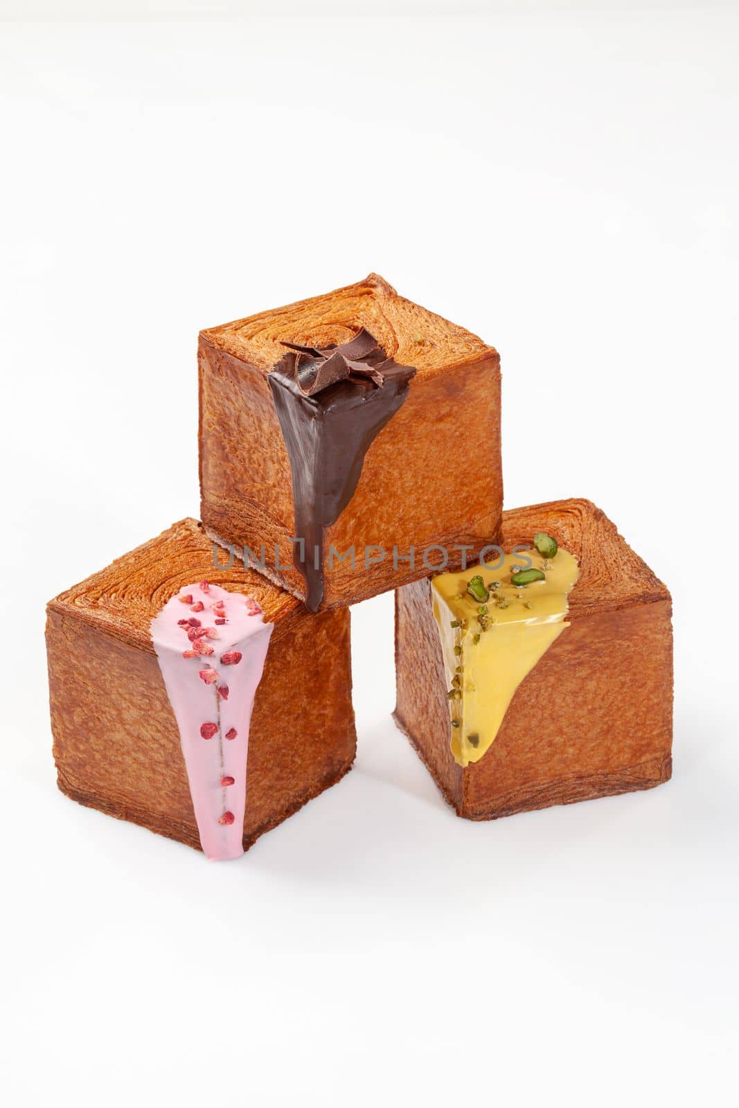 Pyramid of three cubic puff pastry croissants topped with sweet creamy berry sauce, pistachio cream and chocolate glaze isolated on white background. Delicate French style treats