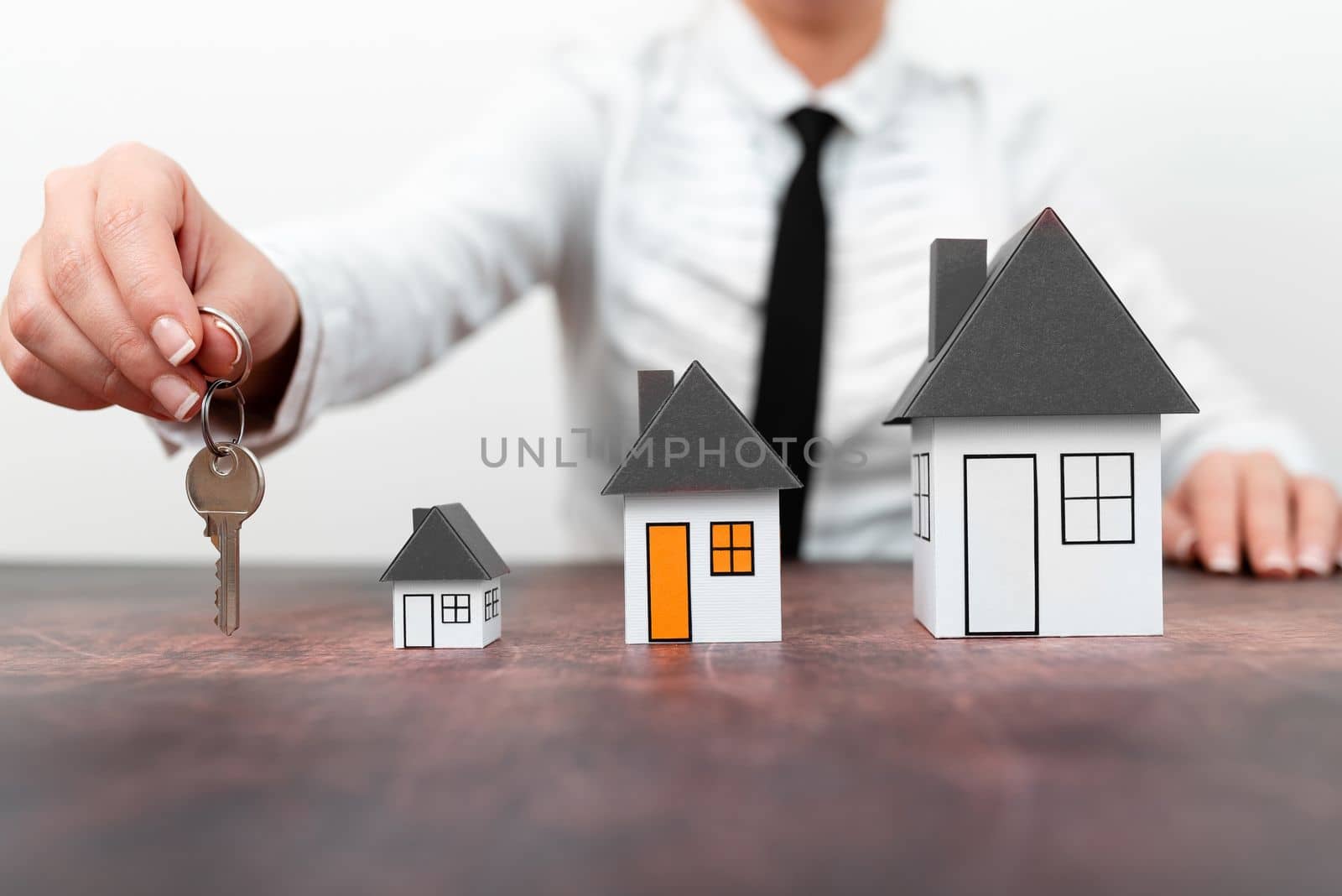 Businesswoman holding keys. olored paper houses standing on desk.