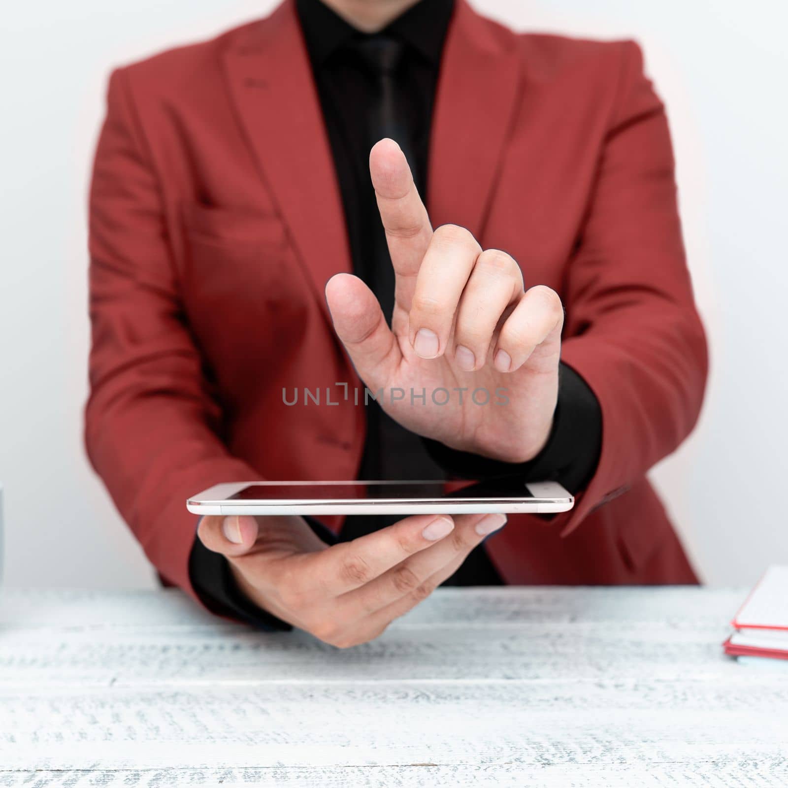 Businessman in Red jacket sitting at table holding mobile phone And Pointing With One Finger On Important Message. Gentleman Showing Critical Announcement. by nialowwa