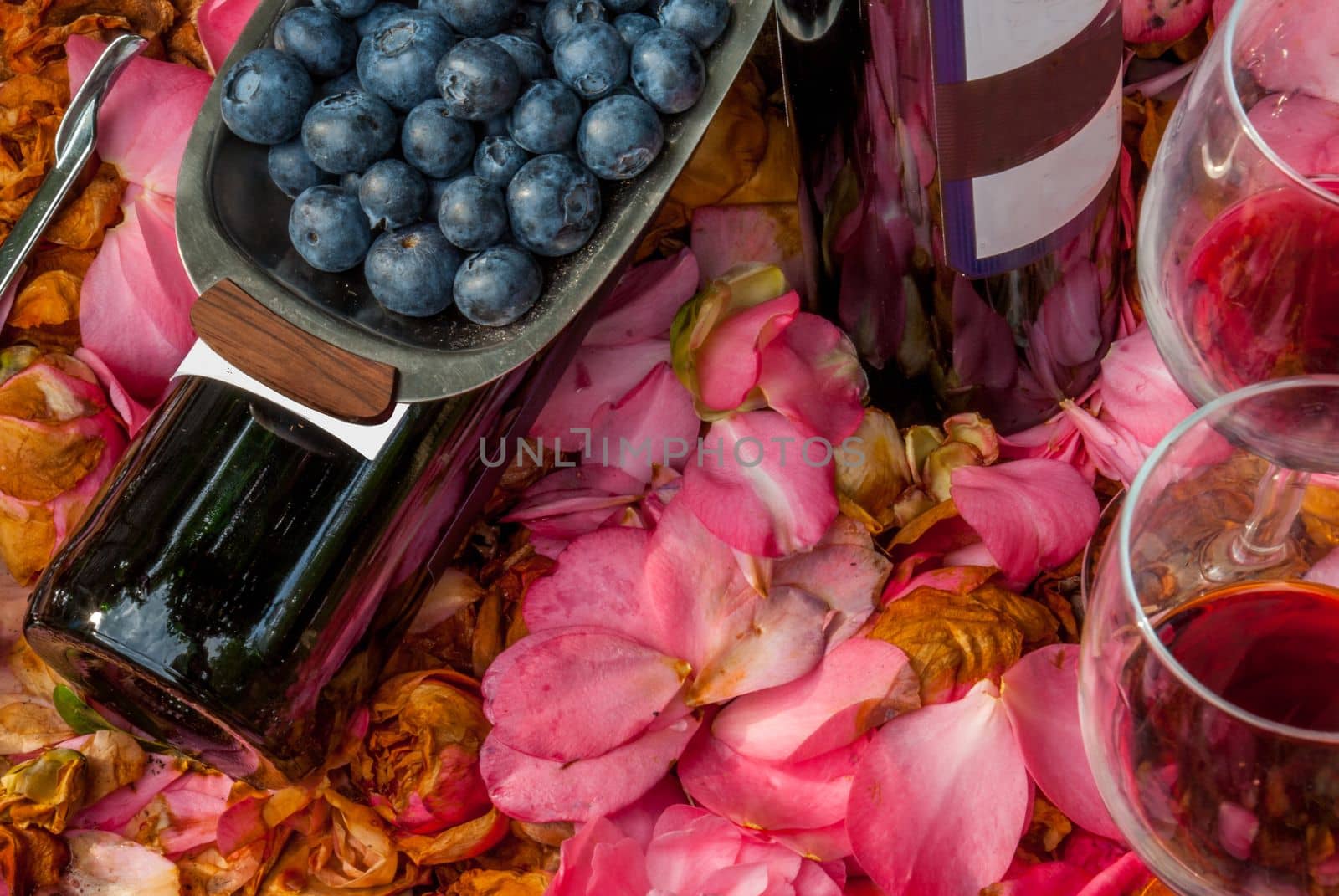 bottles, wine glasses with blueberry in rose garden.