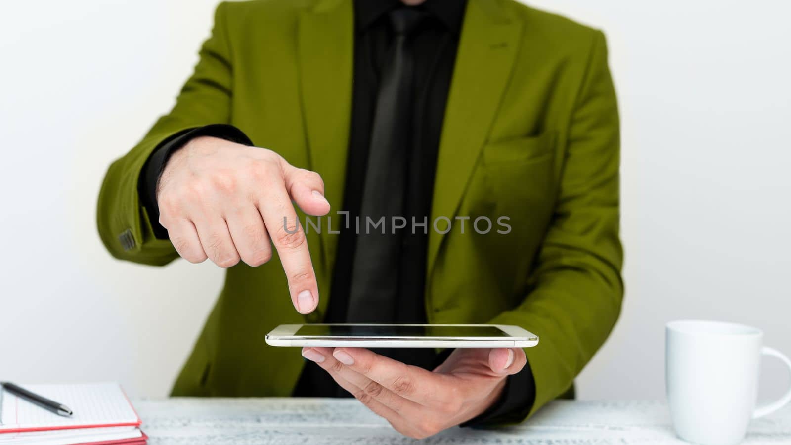 Businessman in Green jacket sitting at table holding mobile phone And Pointing With One Finger On Important Message. Gentleman Showing Critical Announcement. by nialowwa