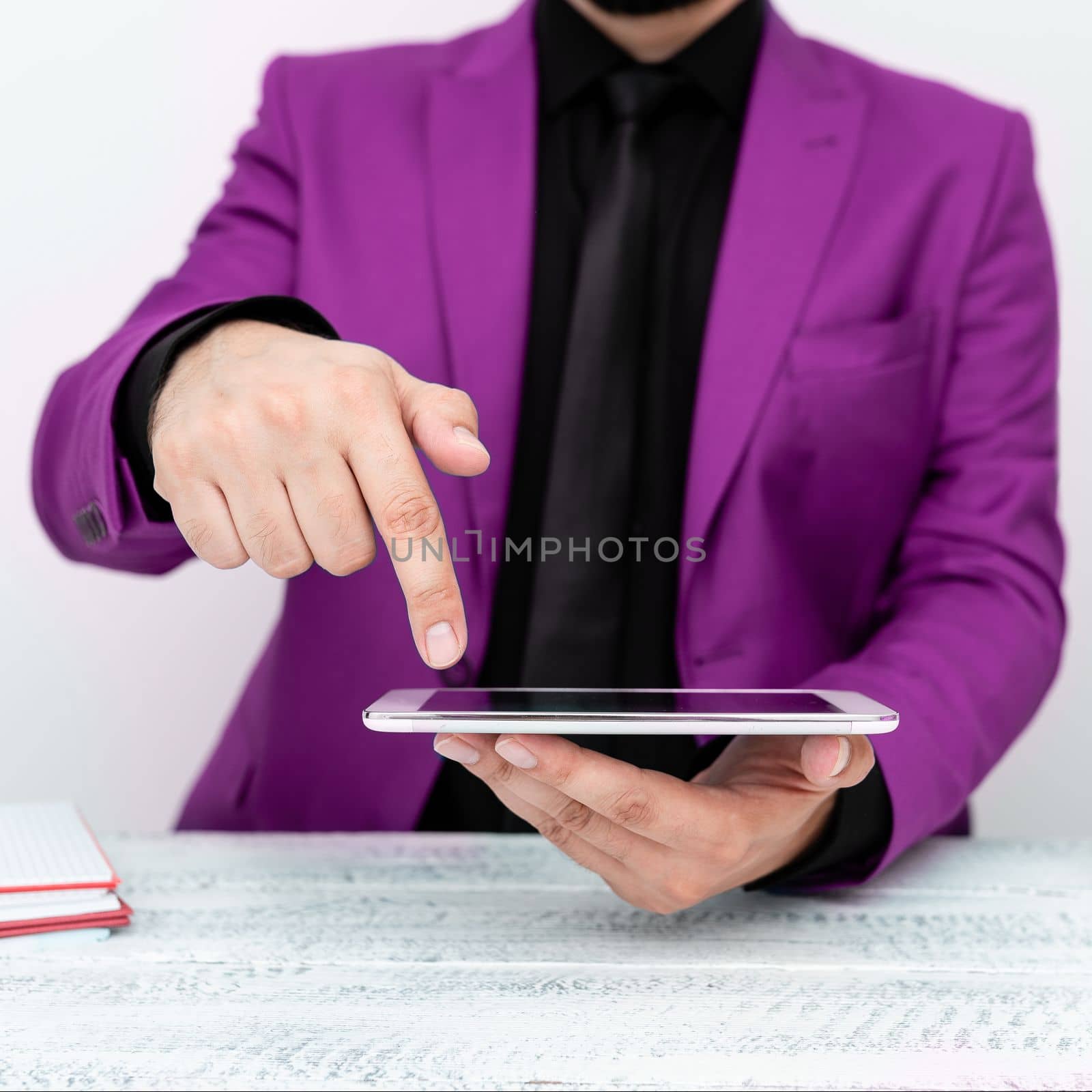 Businessman in Pink jacket sitting at table holding mobile phone And Pointing With One Finger On Important Message. Gentleman Showing Critical Announcement. by nialowwa