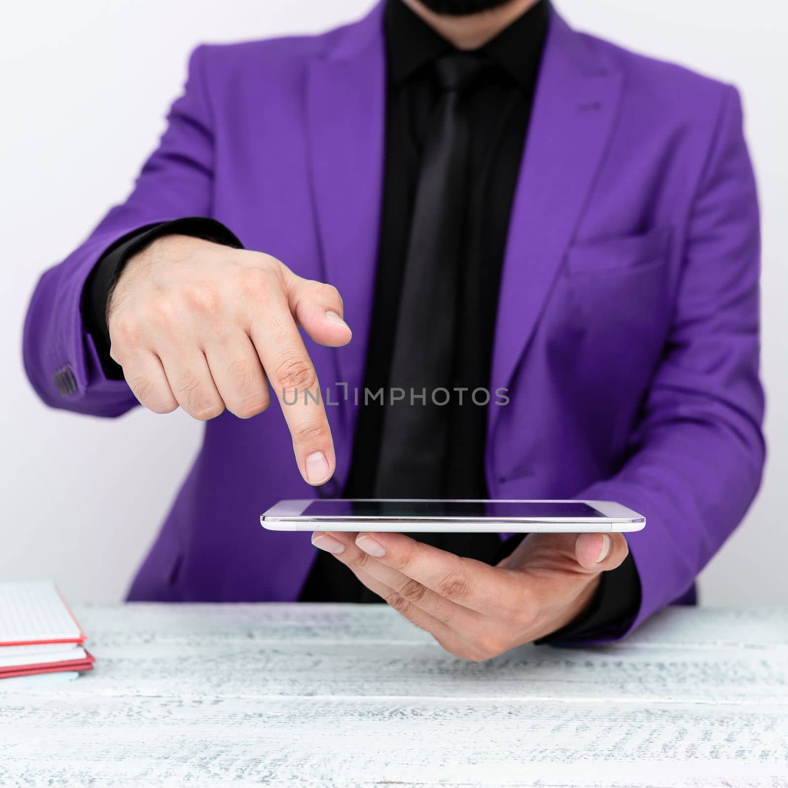 Businessman in Purple jacket sitting at table holding mobile phone And Pointing With One Finger On Important Message. Gentleman Showing Critical Announcement. by nialowwa