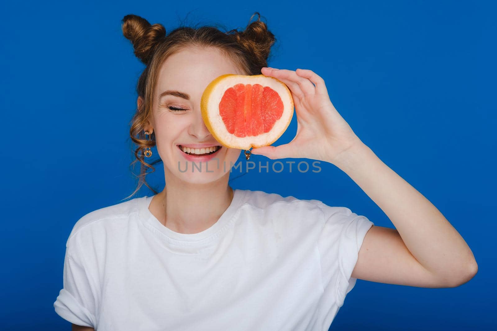 Surprised, the laughing girl holds the grapefruit like ears. Vegan lifestyle. Smiling woman , eating concept.Diet organic , weight loss and healthy food. Smoothies and fresh juice