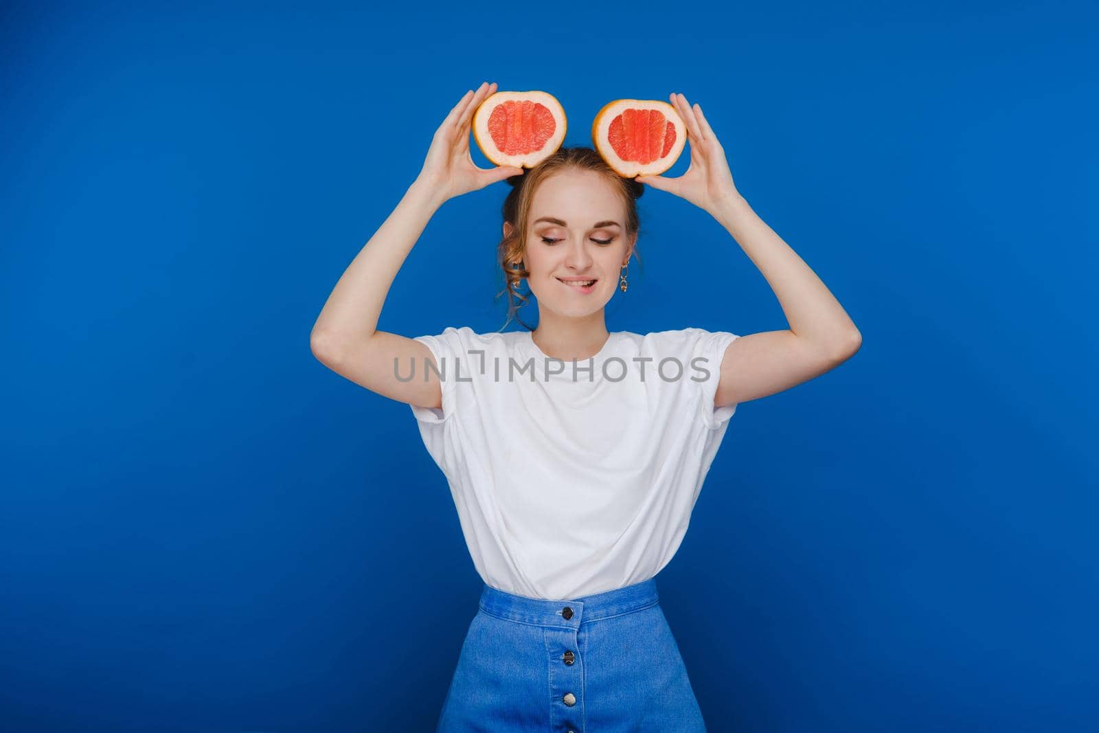 Surprised, the laughing girl holds the grapefruit like ears. Vegan lifestyle. Smiling woman , eating concept.Diet organic , weight loss and healthy food. Smoothies and fresh juice. by Lobachad