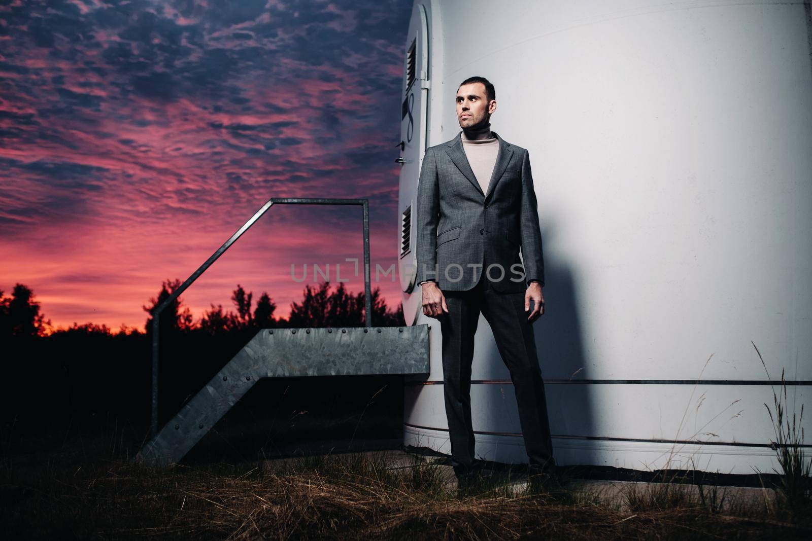 A man in a grey business suit stands next to a windmill after sunset .Businessman near windmills at night.Modern concept of the future