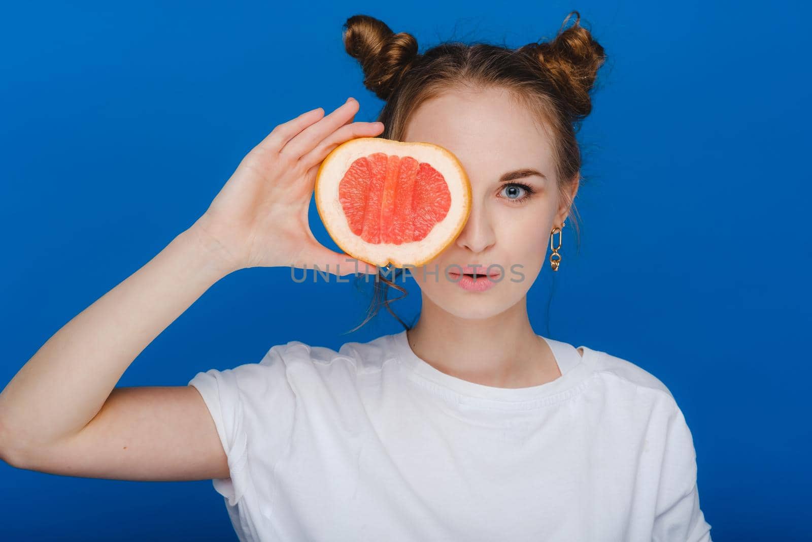 Surprised, the laughing girl holds the grapefruit like ears. Vegan lifestyle. Smiling woman , eating concept.Diet organic , weight loss and healthy food. Smoothies and fresh juice
