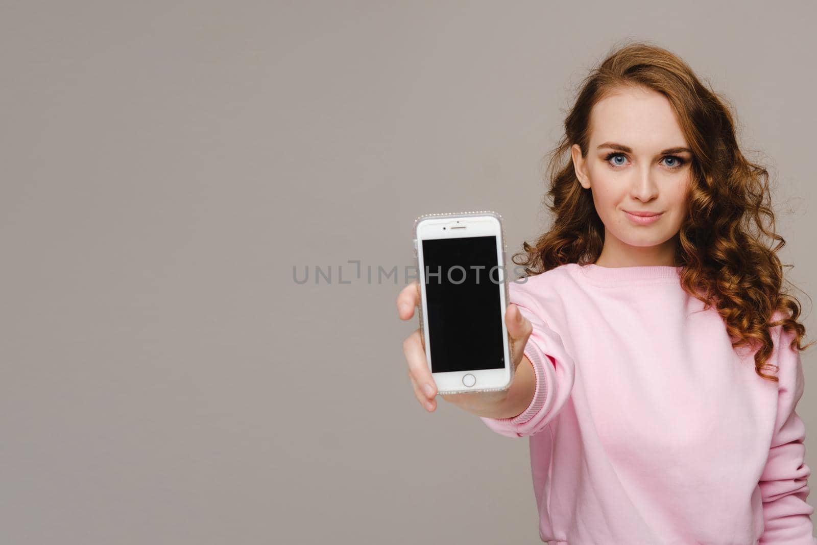 Fashionable girl with a smartphone on the background. Stands and shows the smartphone.