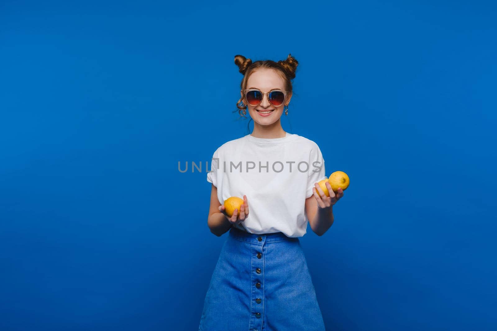 a young beautiful girl standing on a blue background holding lemons in her hand. Smiles.