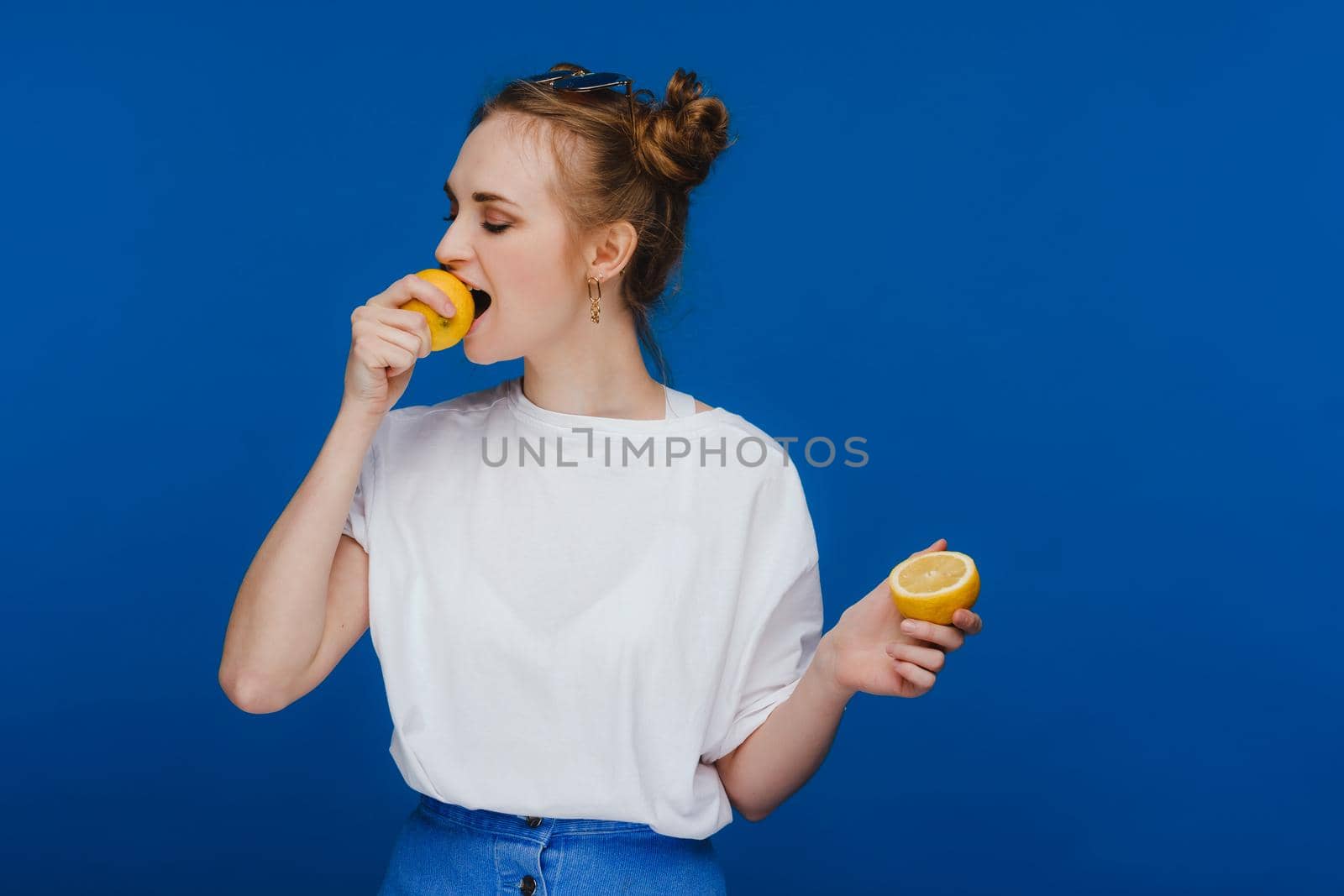 a young beautiful girl standing on a blue background holding lemons in her hand and biting