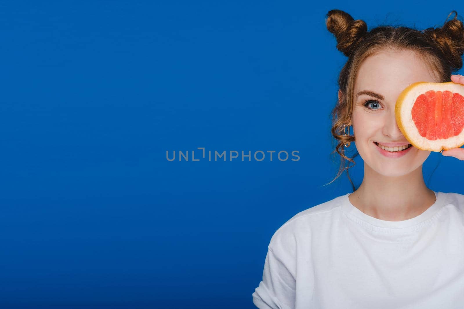 Surprised, the laughing girl holds the grapefruit like ears. Vegan lifestyle. Smiling woman , eating concept.Diet organic , weight loss and healthy food. Smoothies and fresh juice