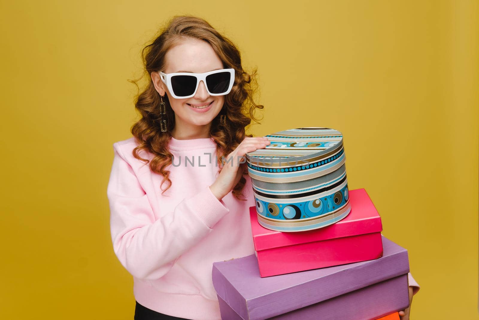 A happy young woman with colorful paper boxes after shopping isolated on an orange Studio background. Seasonal sales, purchases, spending money on gifts by Lobachad