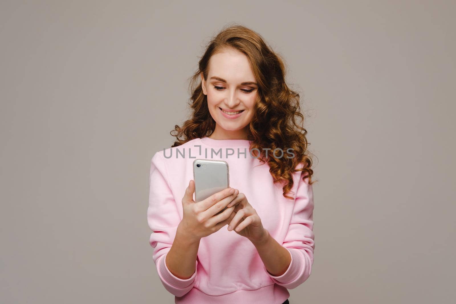 A happy young girl holding a phone looks into it and smiles by Lobachad