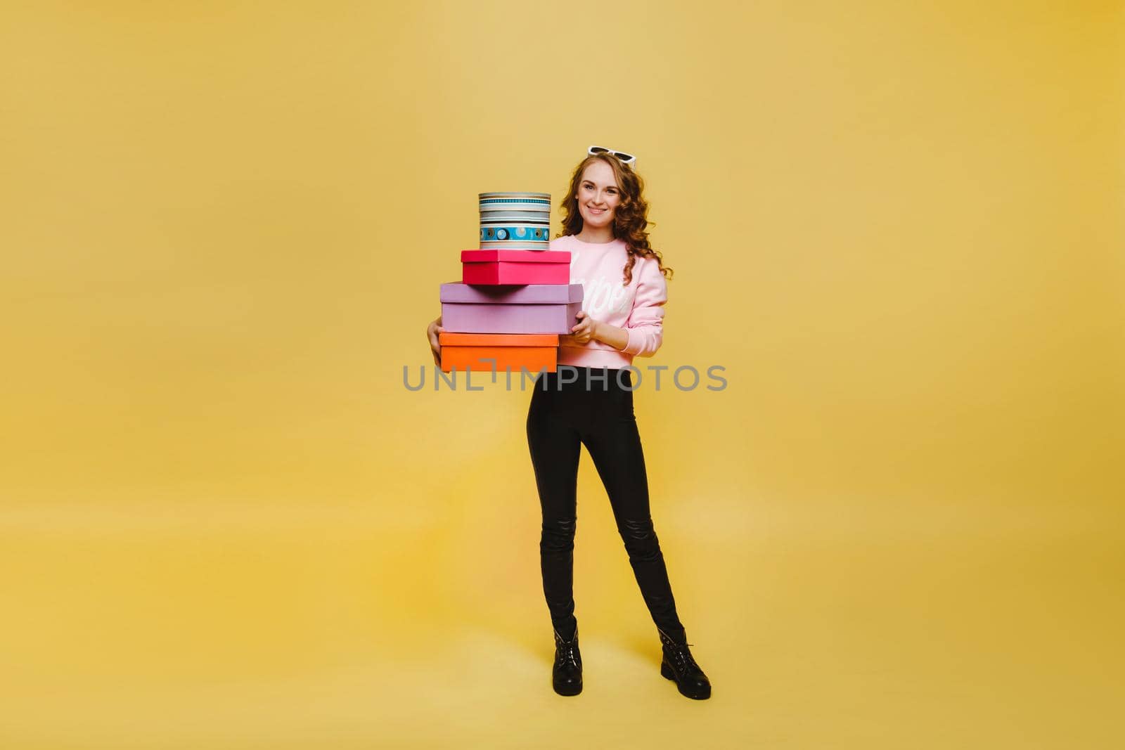 A happy young woman with colorful paper boxes after shopping isolated on an orange Studio background. Seasonal sales, purchases, spending money on gifts by Lobachad