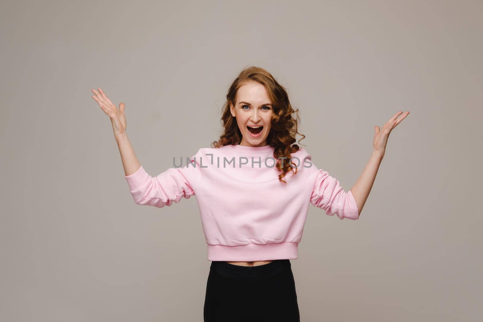 A beautiful girl on a gray background holds her head and screams emotionally.