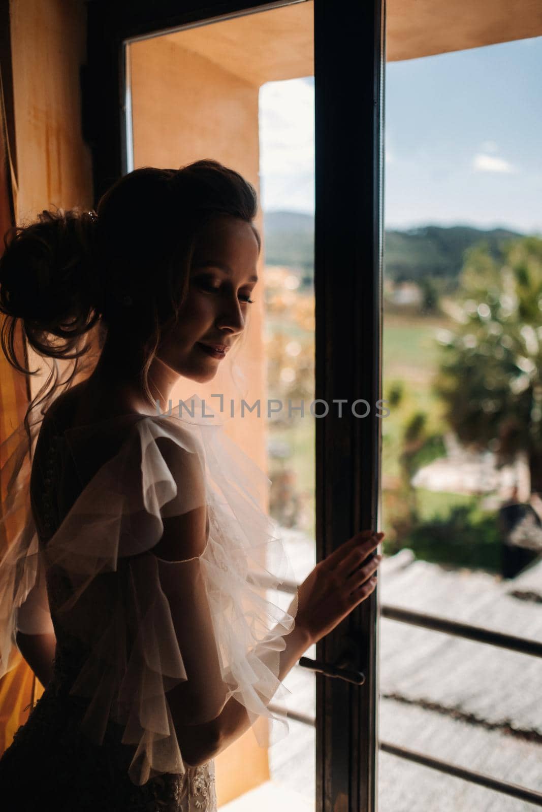 a beautiful bride with pleasant features in a wedding dress poses in the interior of the room. Portrait of the bride in Provence. France by Lobachad