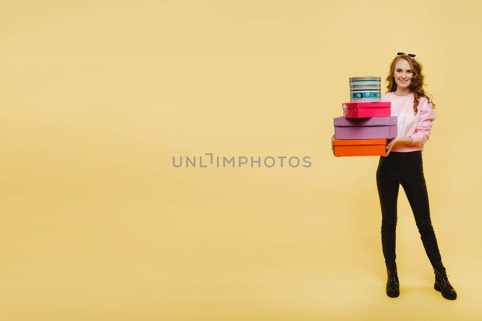 A happy young woman with colorful paper boxes after shopping isolated on an orange Studio background. Seasonal sales, purchases, spending money on gifts.