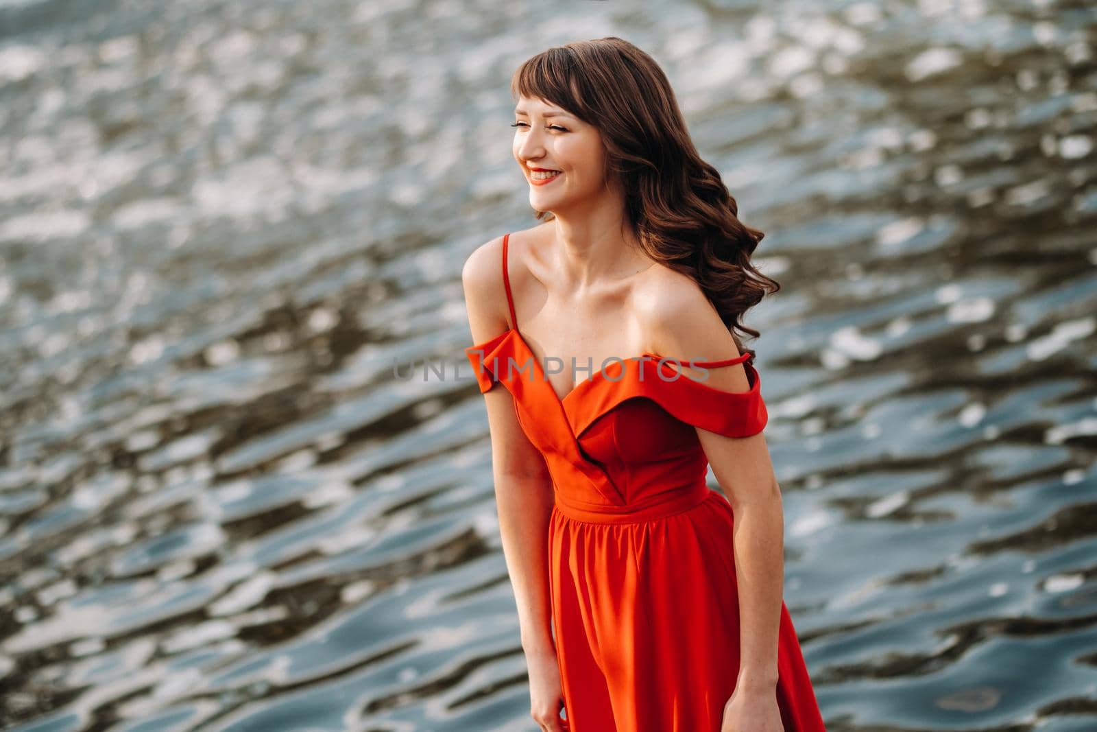 girl in a long red dress near the lake in the Park at sunset