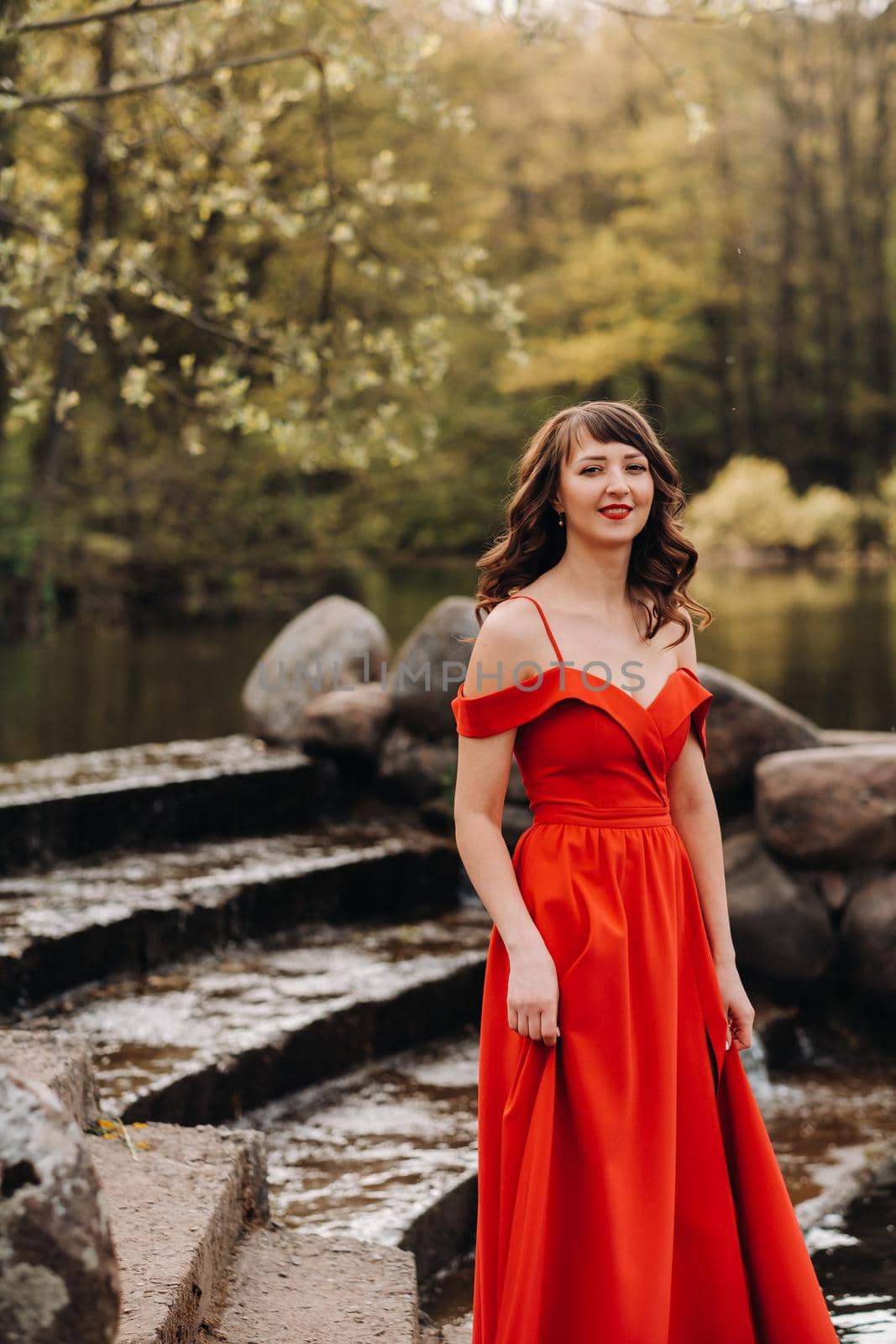 girl in a long red dress near the lake in the Park at sunset. by Lobachad