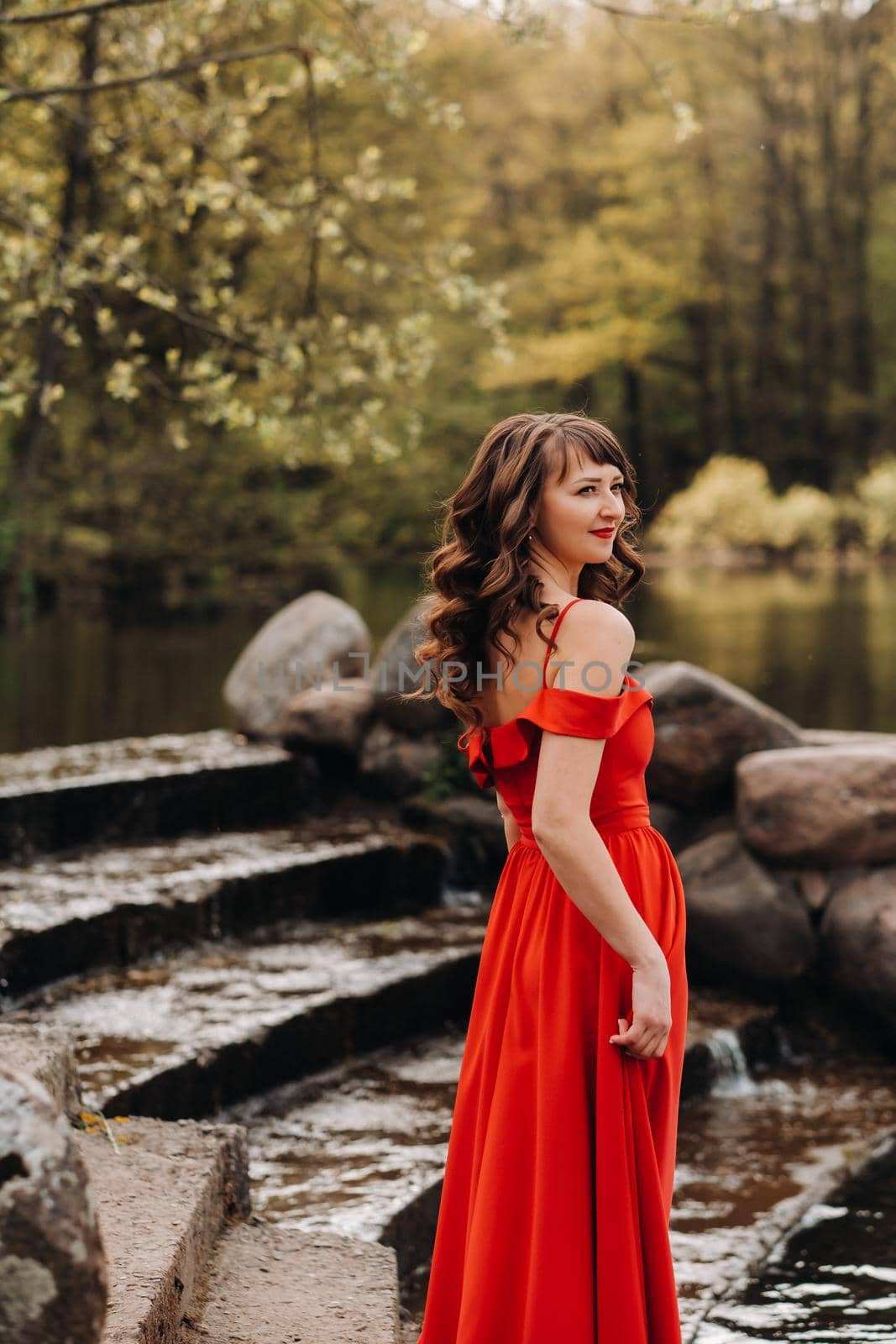 girl in a long red dress near the lake in the Park at sunset