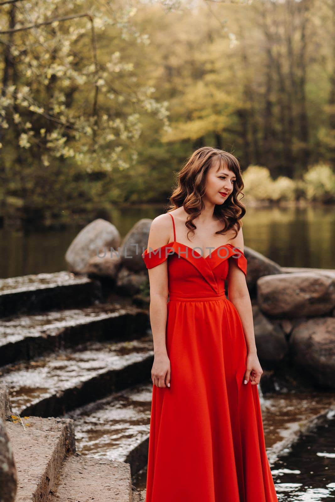girl in a long red dress near the lake in the Park at sunset. by Lobachad