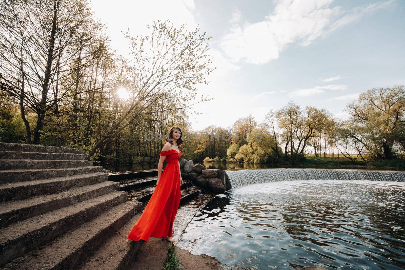 girl in a long red dress near the lake in the Park at sunset