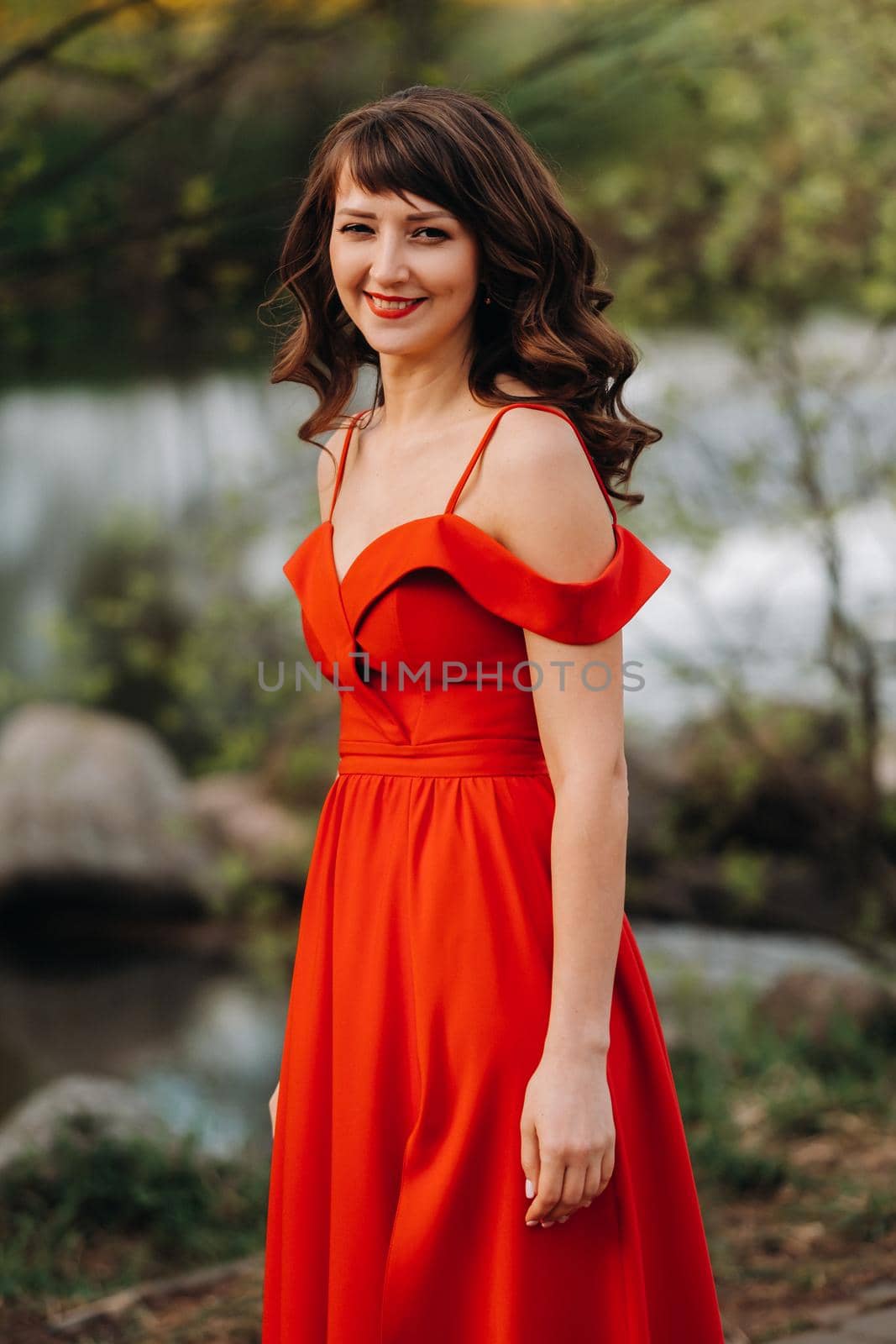 girl in a long red dress near the lake in the Park at sunset