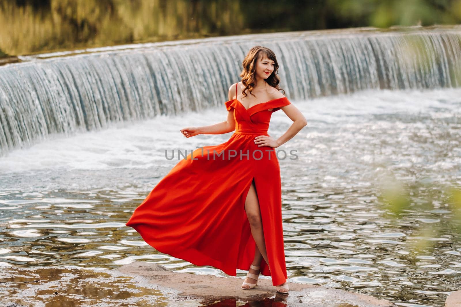 girl in a long red dress near the lake in the Park at sunset