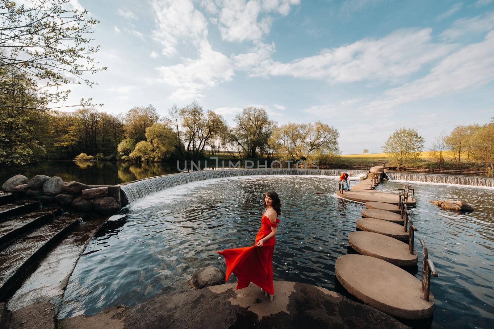 girl in a long red dress near the lake in the Park at sunset. by Lobachad